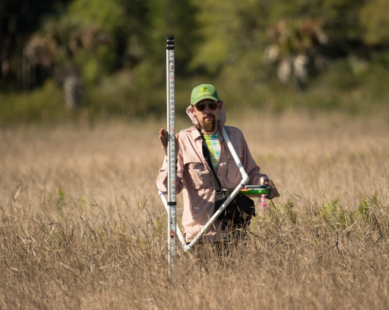 Chance Hines holds a vernier scale within a FL wetland.